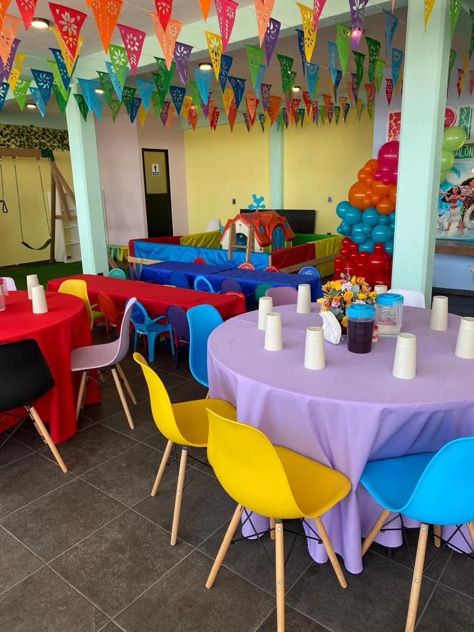 Área de juegos de Perinolita con mesas montadas, resbaladilla, columpios y alberca de pelotas