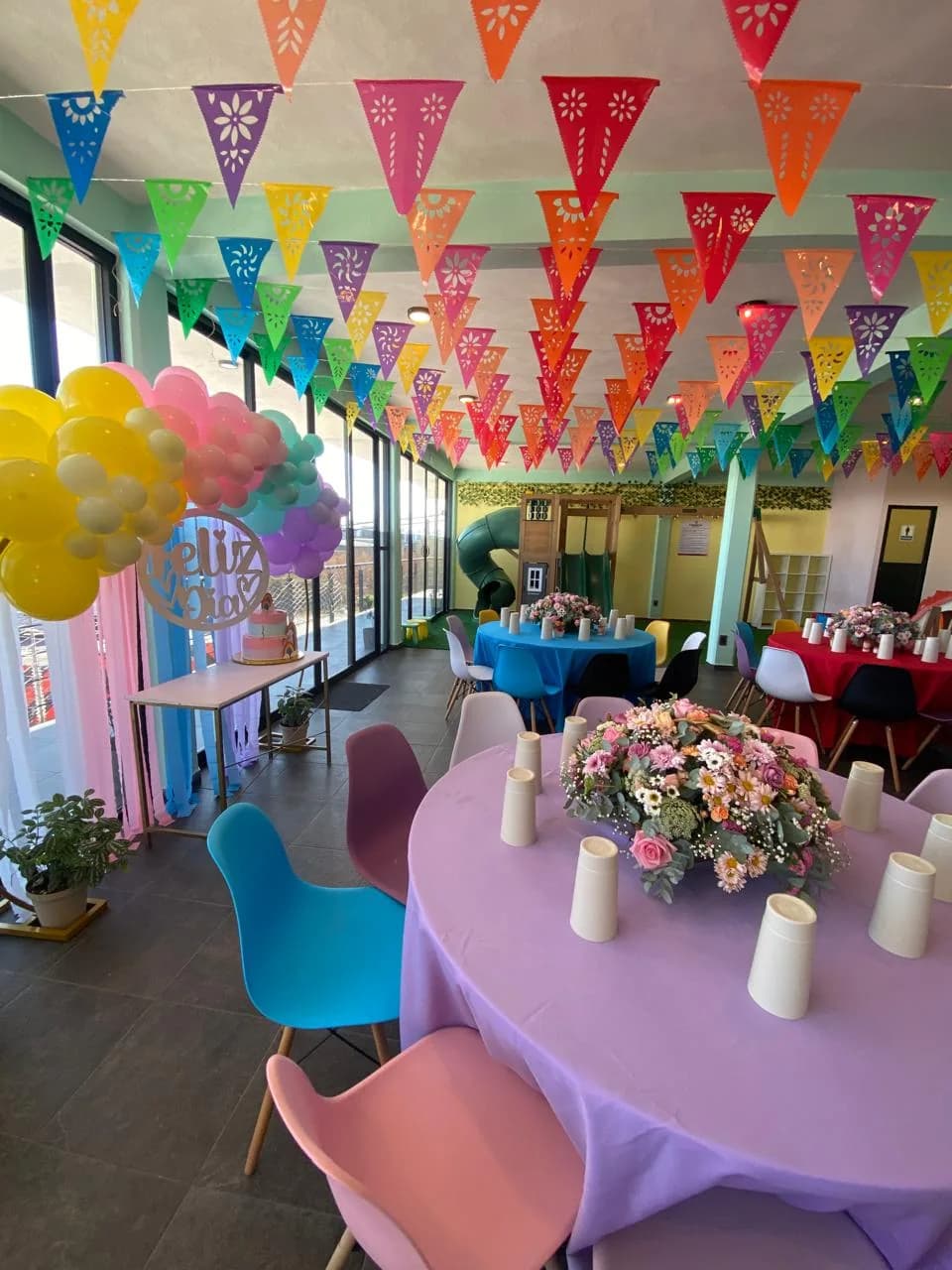 Salón Perinolita montado con mesas de colores, papel picado, arco de globos y área de juegos